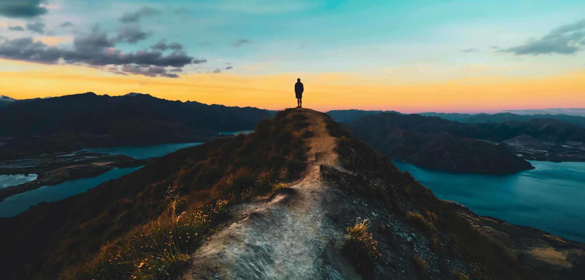 Person silhouetted on Roys Peak with breathtaking sunset view, Wanaka, New Zealand.